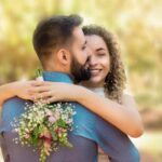 Happy couple embracing with a bouquet in a sunlit garden setting.